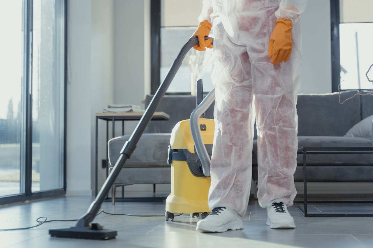 our-experience A cleaner in protective coveralls and gloves vacuuming a modern living room.